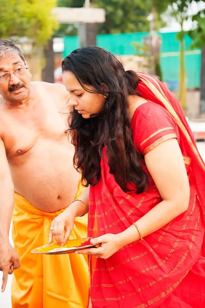 Guruma in a red sari preparing an offering beside Guruji