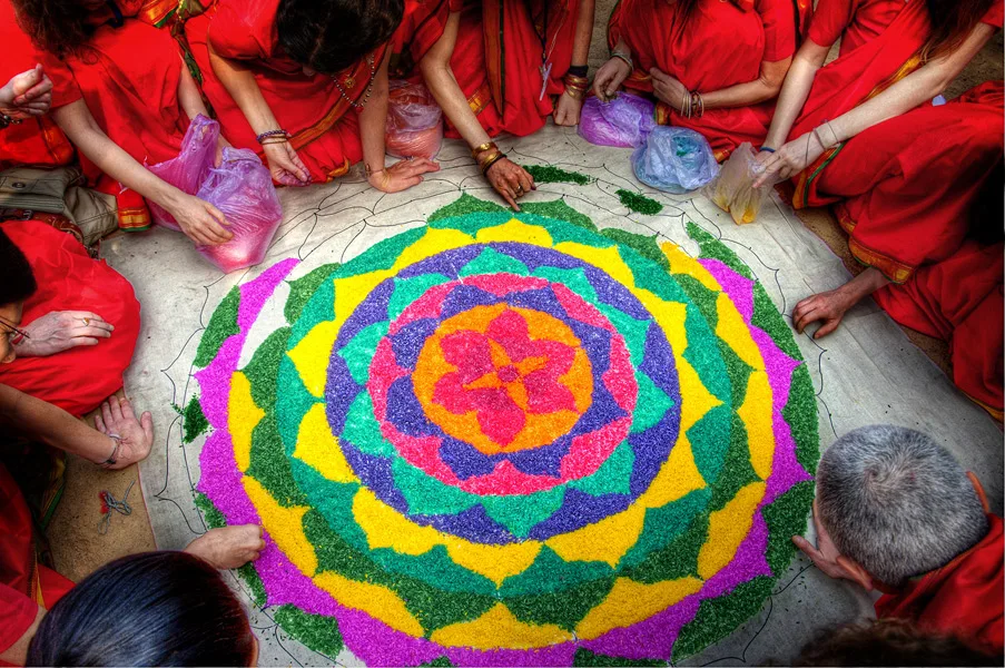 Seen from above: practitioners in red around a yantra of coloured rice